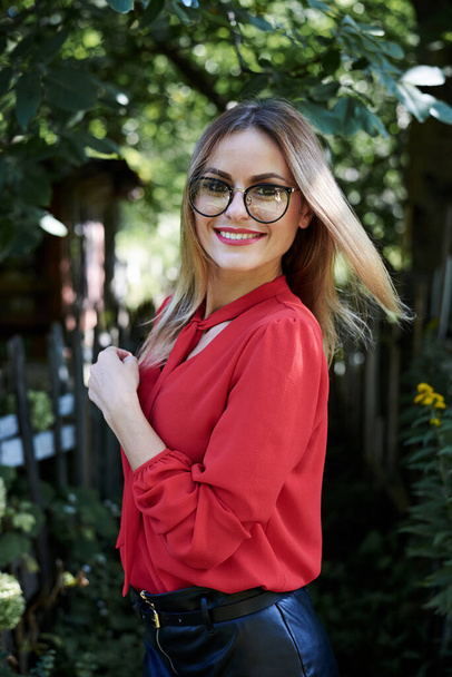 Close-up portrait of attractive young woman with short blond hair, wearing eyeglasses, smiling in the summer garden, Happy female student, posing in the park. Sunny day in campus. - Foto, Imagen