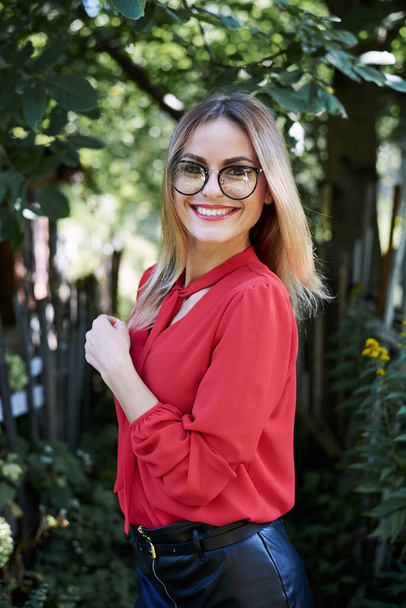Close-up portrait of attractive young woman with short blond hair, wearing eyeglasses, smiling in the summer garden, Happy female student, posing in the park. Sunny day in campus. - Фото, зображення