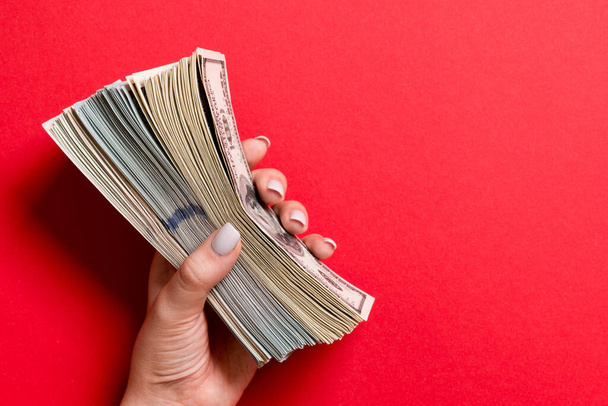 Pohled shora na ženskou ruku držící tlustý balíček různých dolarových bankovek na barevném pozadí. Mzdová a mzdová koncepce s prázdným prostorem pro váš design. - Fotografie, Obrázek