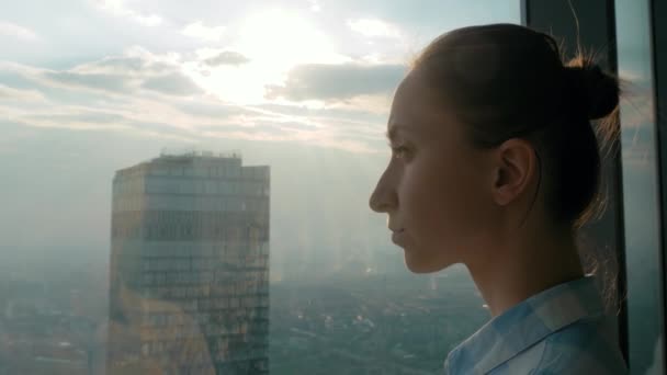 Umsichtige Frau betrachtet Stadtbild durch Fenster des Wolkenkratzers - Seitenansicht - Filmmaterial, Video
