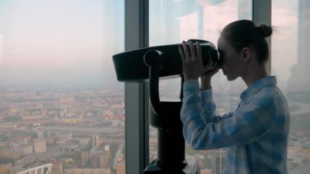 Jonge vrouw op zoek door toeristische telescoop en het verkennen van het stadsgezicht - Video