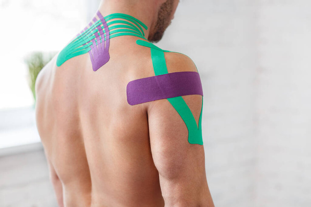 Kinesiology taping. Kinesiology tape on patient neck. Injured trapezius muscles treatment of young male athlete. Post traumatic rehabilitation, sport physical therapy, recovery concept - Fotografie, Obrázek