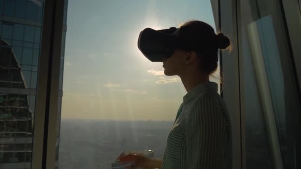 Gökdelen penceresine karşı sanal gerçeklik kulaklığı kullanan genç kadın - VR kavramı - Video, Çekim