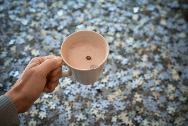 Hand holds a cup of milk with cocoa on a background of puzzle pieces, Stay at home - Photo, Image