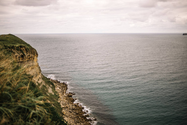 Maritime horizon view with cliff, grass, rocks and cloudy sky in Cantabria, Spain - Foto, imagen