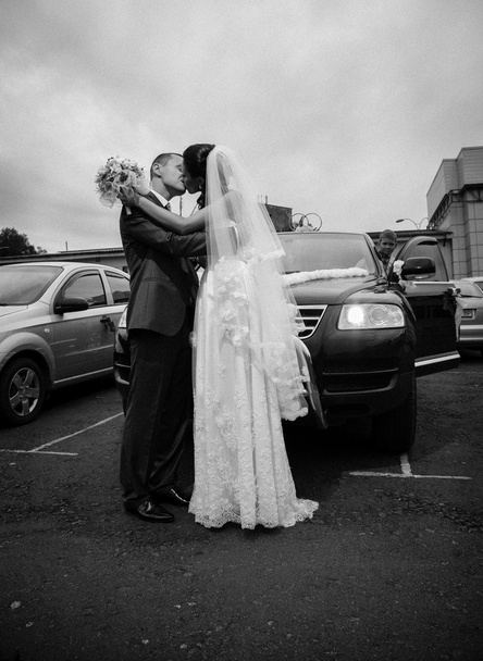 νιόπαντρο ζευγάρι φιλιά στάθμευσης κατά μαύρο αυτοκίνητο - Φωτογραφία, εικόνα
