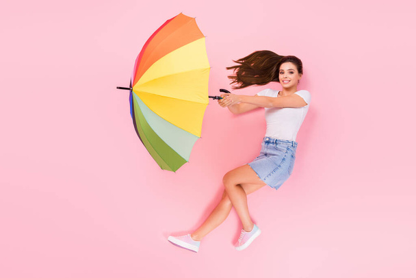 Top above high angle view full length profile side photo of positive girl hold umbrella fly air wind blow lay enjoy rainy weather wear style outfit isolated over pastel color background - Photo, image
