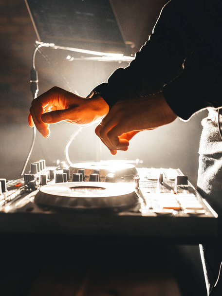Πλευρική άποψη των αρσενικών χεριών DJ, που παίζουν σε κονσόλα ανάμειξης, με λευκά κρύα φώτα και καπνό στον αέρα - Φωτογραφία, εικόνα