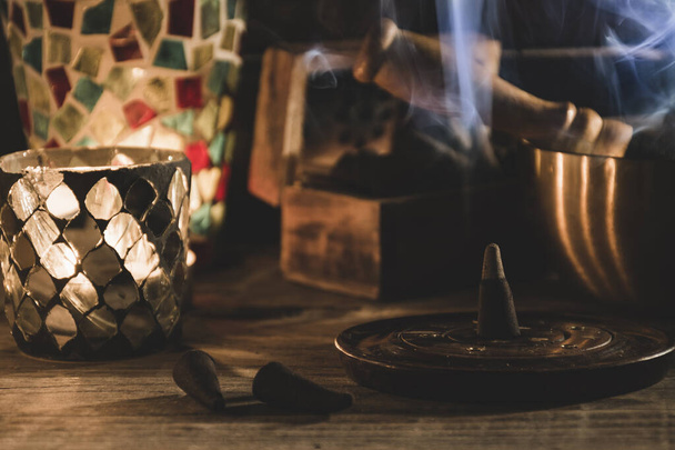 Lighted incense cone next to a Tibetan bowl and some candles. Blue smoke. Meditation, yoga, calm, healing and religion concepts. Dark style. Horizontal - Fotografie, Obrázek