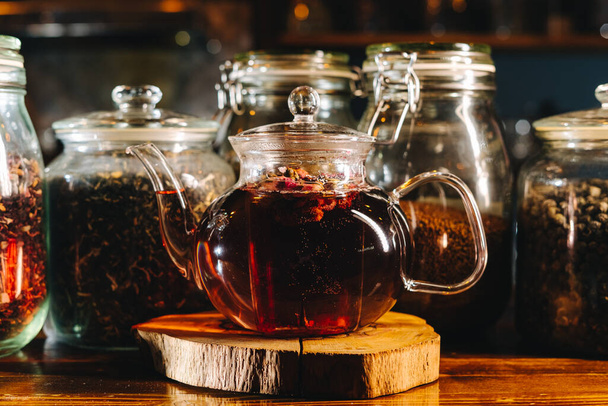 Czajniczek czarnej herbaty stojący przed słoikami wypełnionymi liśćmi herbaty, ciepłe światło, zbliżenie - Zdjęcie, obraz