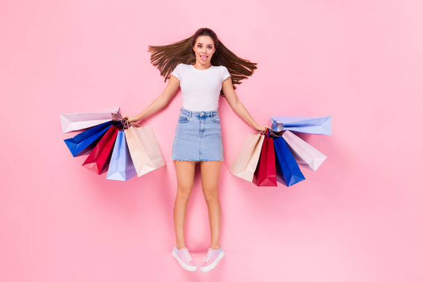 Top above high angle view full size photo of childish playful girl lay have shopping rest hold bags show tongue out wear white t-shirt isolated over pastel color background - Foto, Imagen