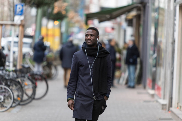 Junger schwarzer Mann mit Kopfhörer und Wintermantel läuft auf die Straße und schaut weg.  - Foto, Bild