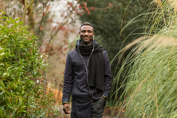 Jonge zwarte man glimlachend oprecht staand in het herfstpark.  - Foto, afbeelding