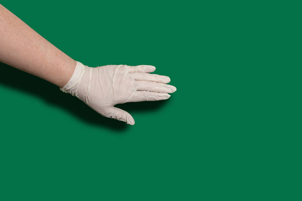 Female hand in sterile latex gloves on a green background with copy space. Hygiene and virus protection concept - Fotó, kép