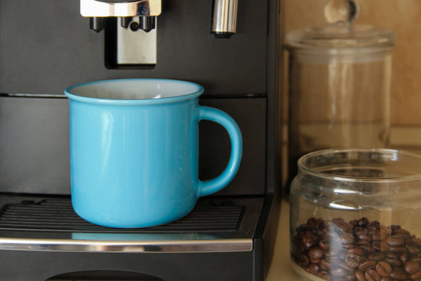 キッチンにはブルーコーヒーマグカップとコーヒーメーカーが立っています。プロのコーヒーブレンド機.  - 写真・画像