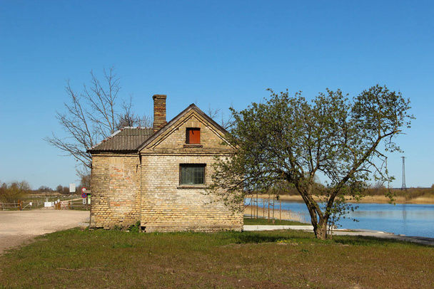 Pequeña y vieja casa de ladrillo con una chimenea cerca de un canal. Lugar idílico para vivir cerca del río
. - Foto, Imagen