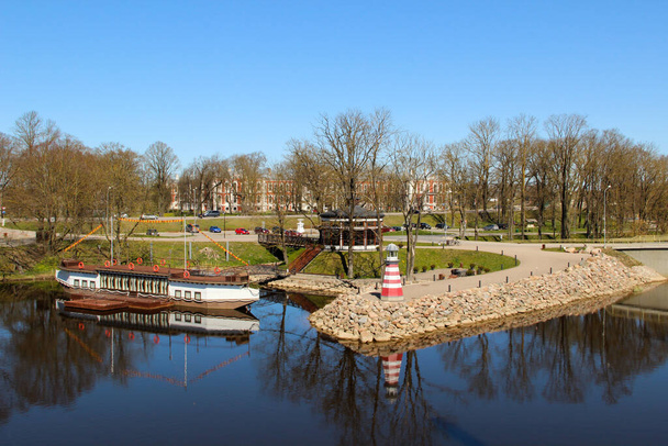 Stadtkanal mit kostspieligem Leuchtturm und Flussboot an der Küste. Beliebte Wasserlandschaft in der Stadt Jelgava.  - Foto, Bild