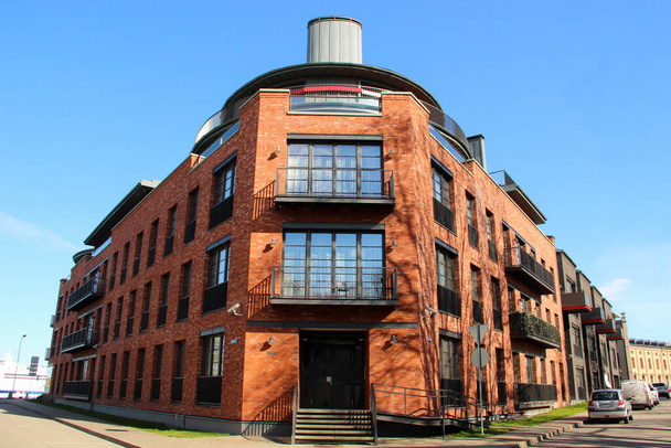 Moderne Wohnungen in dem aus roten Ziegeln erbauten Haus. Hausecke mit Balkonen über Eingangstür. - Foto, Bild