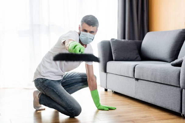 Selective focus of man in medical mask and rubber gloves holding broom at home  - Foto, Bild