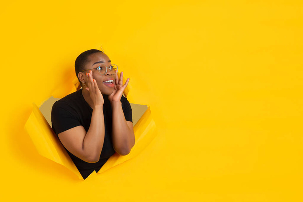 Cheerful young woman poses in torn yellow paper hole background, emotional and expressive, shouting with speaker - Fotó, kép