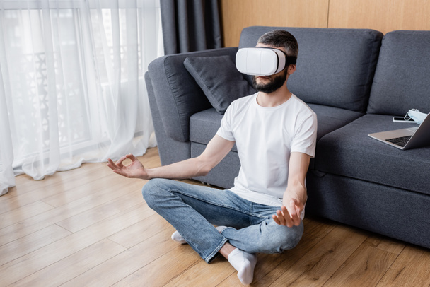 Férfi vr headset meditál lótuszban pózol a padlón a nappaliban - Fotó, kép
