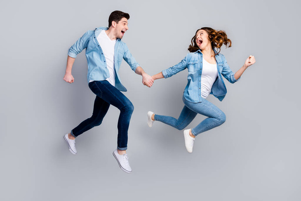 Full size photo of cheerful funky students spouses enjoy spring weekend rest jump hold hand run moving wear casual style outfit gumshoes isolated over gray color background - Foto, Imagem