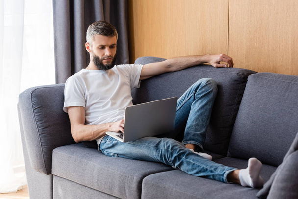 Handsome man working on laptop on couch at home  - Photo, Image