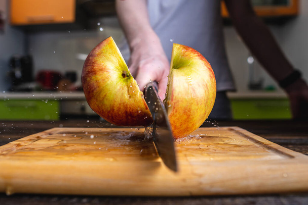 Chef cutting a yellow ripe apple in half with a large knife in motion. Splashes of water and juice fly in different directions and freeze in the air - Fotó, kép