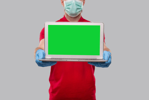 Доставщик несет медицинскую маску и глотки, прикрывающие верхний зеленый экран. Домашние заказы, доставка карантина, покупки онлайн, концепция фрилансера. Isolated
 - Фото, изображение