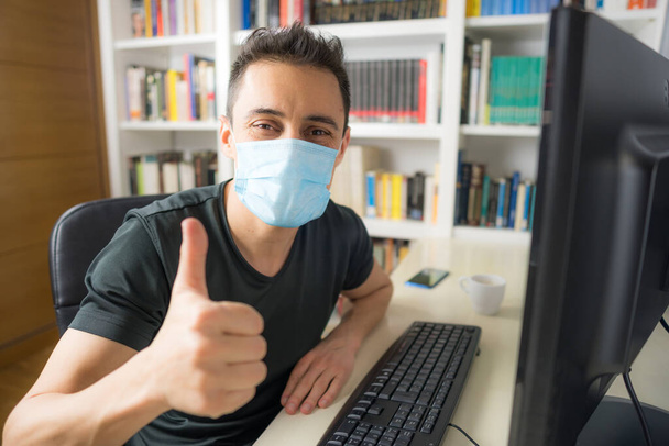 Man teleworking at home, sitting in front of the computer wearing a shirt and mask. Mid shot. - Photo, Image