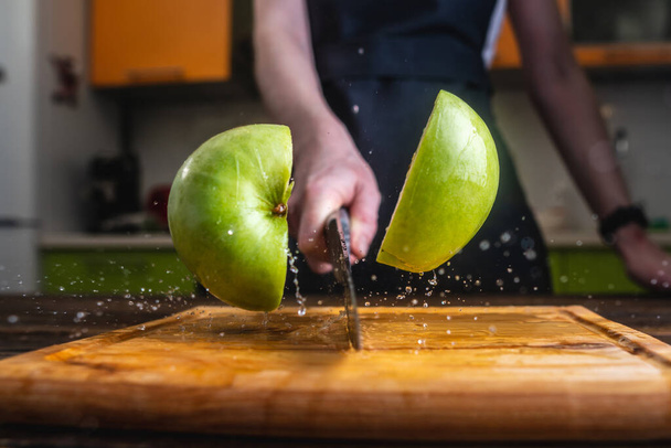 Шеф-кухар розрізає зелене яблуко навпіл з великим ножем у русі. Подрібнення води і соку літають в різних напрямках і замерзають у повітрі
 - Фото, зображення