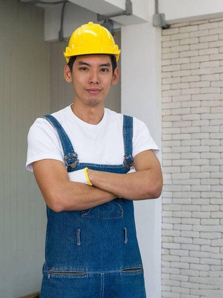 Un carpintero asiático vistiendo un sombrero amarillo, de pie cruzó los brazos en la sala de taller
.  - Foto, Imagen