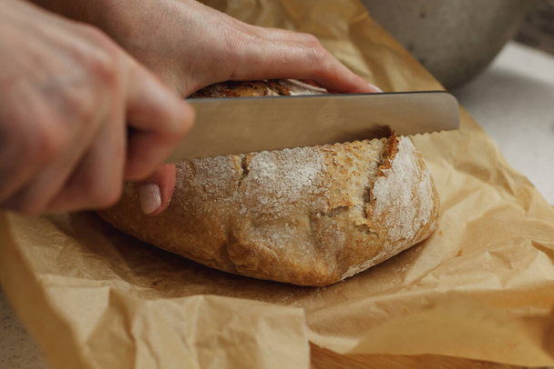 Hands of a woman cutting a piece of freshly baked bread - Zdjęcie, obraz