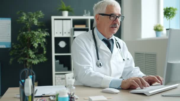 Medical specialist in uniform working with computer typing in clinic office - Materiał filmowy, wideo