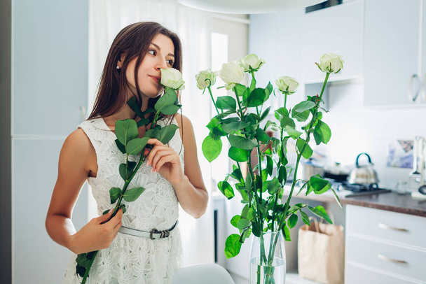 Woman puts roses in vase smells flowers at home. Housewife taking care of comfort on kitchen on quarantine isolation. Interior design - Photo, Image