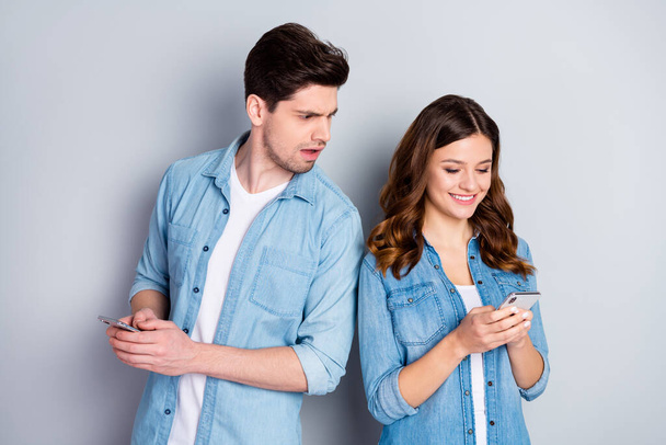 Photo pretty funny lady handsome suspicious guy boyfriend look her telephone read other guy sms cheating lover wear casual denim shirts outfit isolated grey color background - Foto, Bild