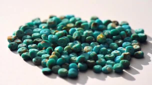 A natural turquoise stone close-up in form of a heap or slide is spinning on a light gray metal background. Natural turquoise stones to create jewelry. Natural stones and minerals. Collection stones. - Footage, Video