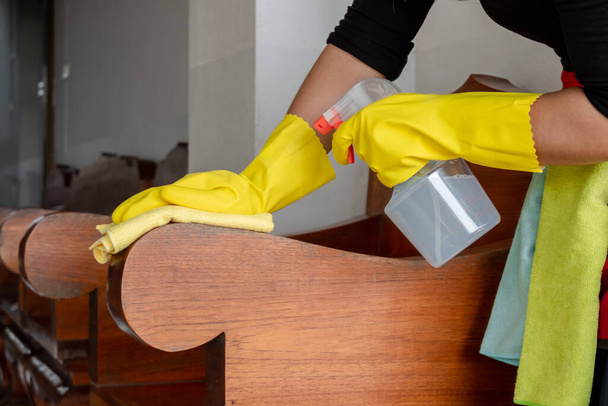 Les femmes au foyer heureuses dans des gants en caoutchouc essuient la poussière avec un spray tout en nettoyant les tables et les chaises concept de nettoyage
. - Photo, image