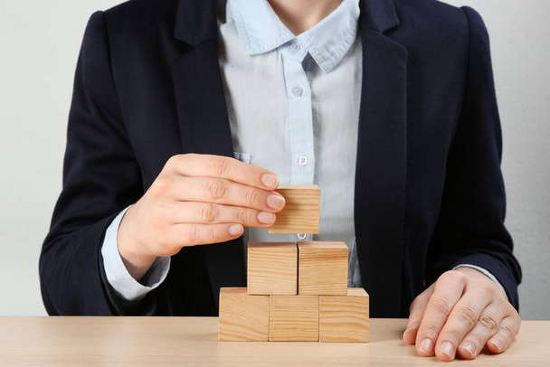 Woman building pyramid at wooden table, closeup. Career promotion concept - Foto, afbeelding