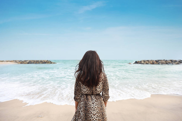 Rear view happiness traveller young asian woman in beautiful dress standing on sandy beach. Cute girl enjoy her tropical sea on her holiday vacation during summer time and sunshine day. - Foto, immagini
