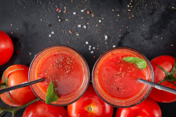 2 glasses of tomato juice with mint and spices, salt, pepper and tubes, fresh red tomatoes on a black , top view,  - Фото, зображення