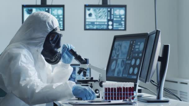 Wetenschapper in beschermingspak en maskers die in onderzoekslaboratorium met behulp van laboratoriumapparatuur werken: microscopen, reageerbuizen. Coronavirus 2019-ncov hazard, farmaceutische ontdekking, bacteriologie en virologie - Video