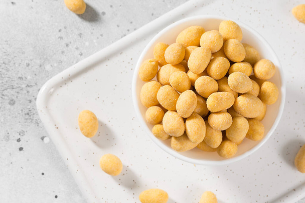 Grilled peanuts in cheese sauce in a white bowl on a light gray table. The view from the top. Close-up with space for text - Foto, afbeelding