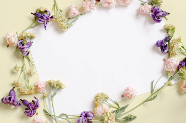 Frame of flowers close-up on a yellow background. Floral background with place for your text. Pastel colors. A piece of white paper in a floral frame. - Photo, Image