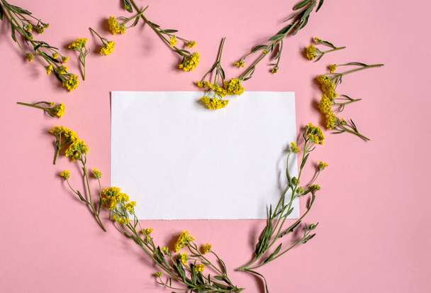 Λευκό σεντόνι σε ροζ φόντο. Ένα κομμάτι λευκό χαρτί σε ένα πλαίσιο από λουλούδια. Λουλούδια με τη μορφή καρδιάς. - Φωτογραφία, εικόνα