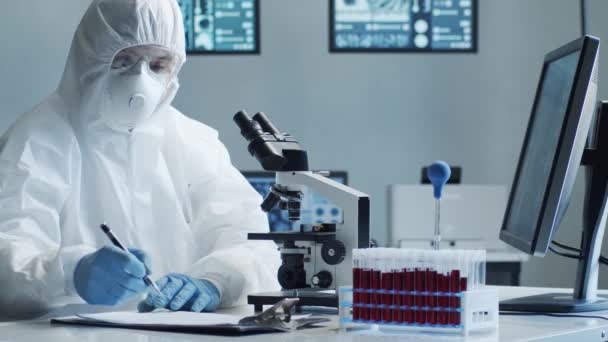 Vědec v ochranných oblecích a maskách pracující ve výzkumné laboratoři pomocí laboratorního vybavení: mikroskopy, zkumavky. Koronavirus covid-19 nebezpečí, farmaceutický objev, bakteriologie a virologie - Záběry, video