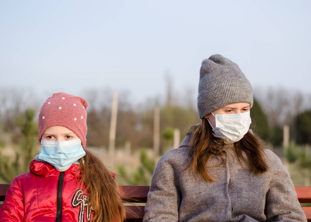 ベンチの上の公園で医療用マスクの娘とお母さん。コロナウイルス対策マスク。COVY-19 。若いです女の子とともに子供で医療マスク - 写真・画像