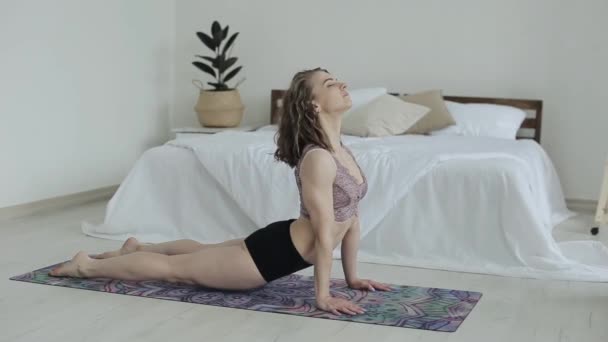 Młoda piękna dziewczyna ćwiczy jogę pozuje leżąc na macie w swoim pokoju w sportowym staniku i bieliźnie. Kobieta uprawiająca jogę w domu podczas kwarantanny. - Materiał filmowy, wideo