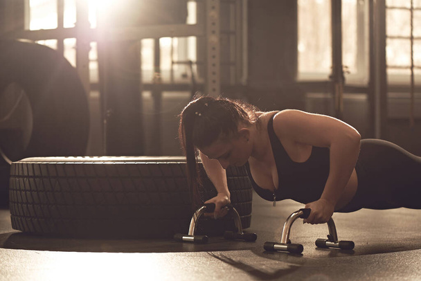 Young woman does push-ups with sports equipment in the gym. Real Workout Candid fitness Girl - Photo, Image