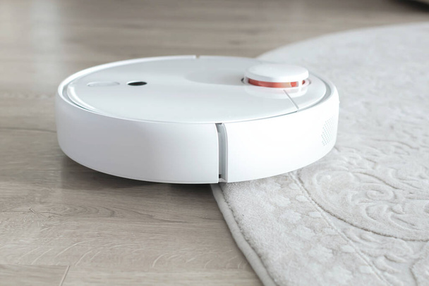 Valkoinen robotti imuri lattialla. Moderni älykäs laite puhdistus lattia
. - Valokuva, kuva